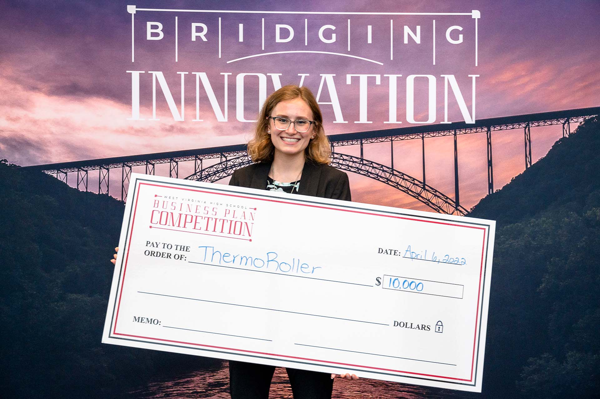 A smiling woman wearing glasses holding a large check in front of a backdrop