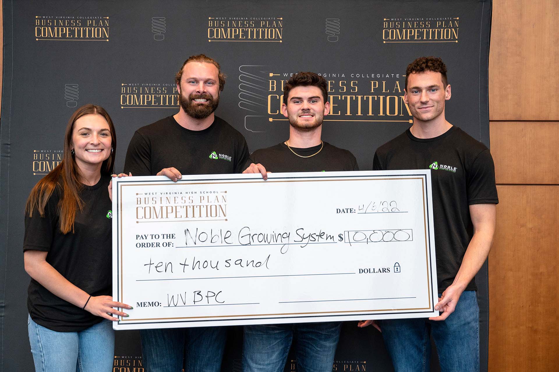 Four smiling people holding a large check in front of a backdrop